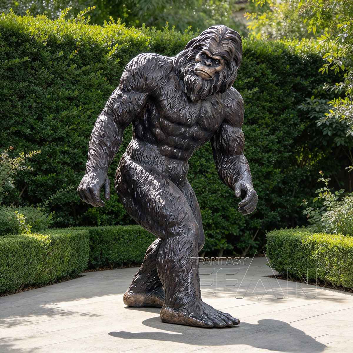 Dark bronze Bigfoot statue displayed on a garden path with green hedges