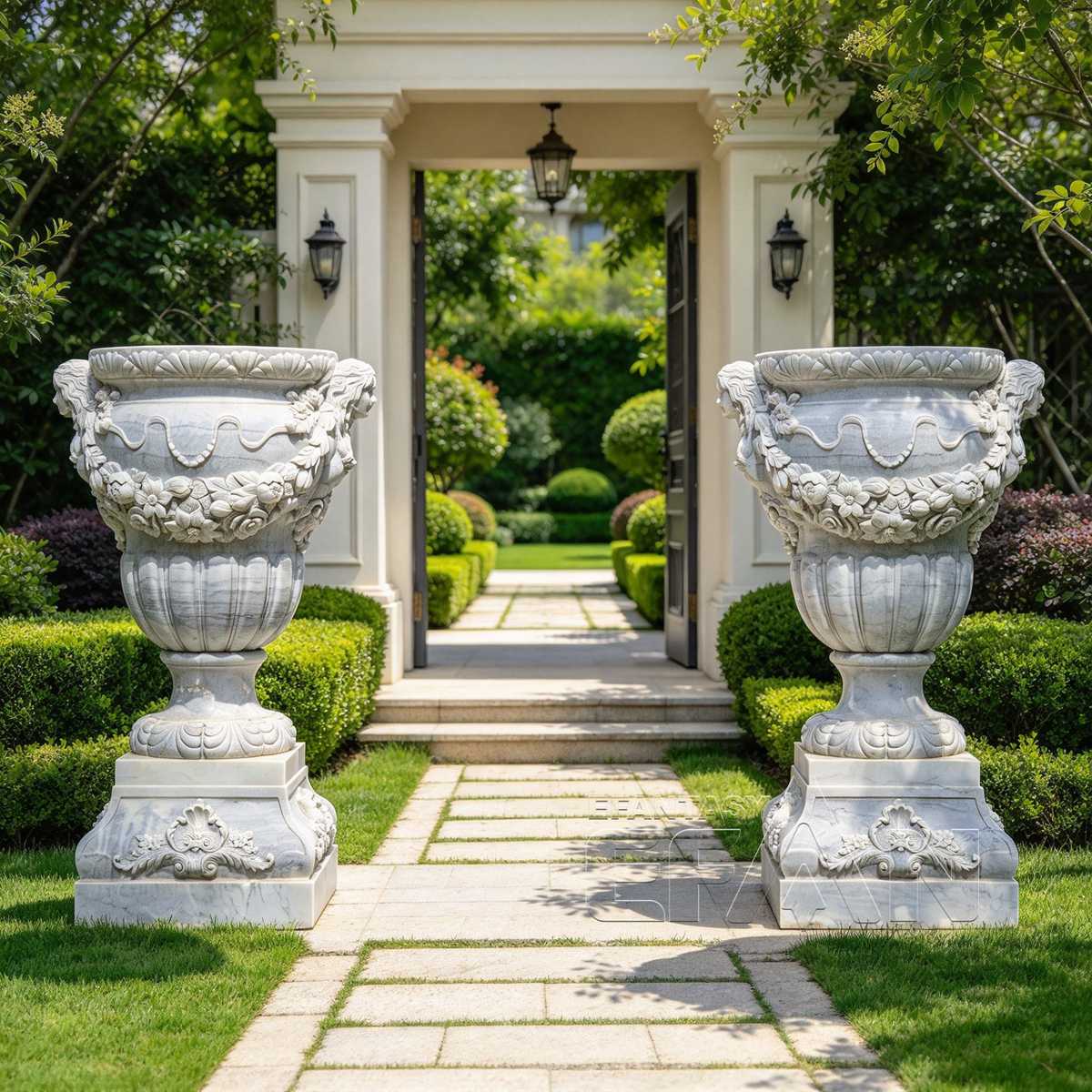 Matching white marble urn planters with carved garlands flanking a garden entrance