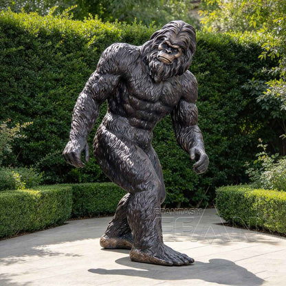 Dark bronze Bigfoot statue displayed on a garden path with green hedges