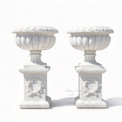 Two white marble fluted urn planters with carved laurel wreath pedestals on a white background