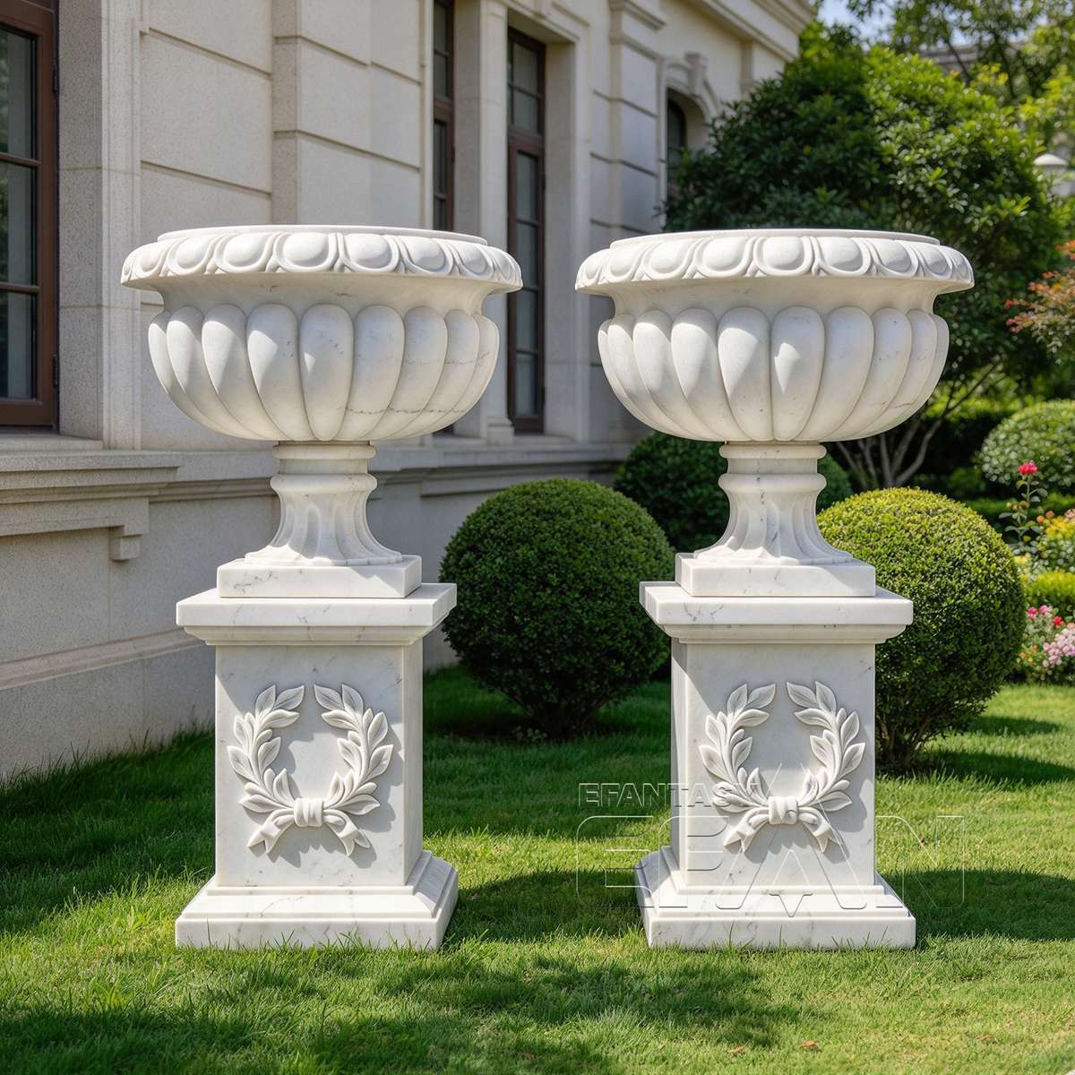 White marble urn planters with laurel wreath pedestals beside a classical estate