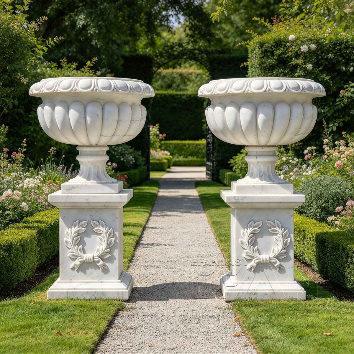 Matching white marble urn planters with laurel wreath bases framing a garden walkway