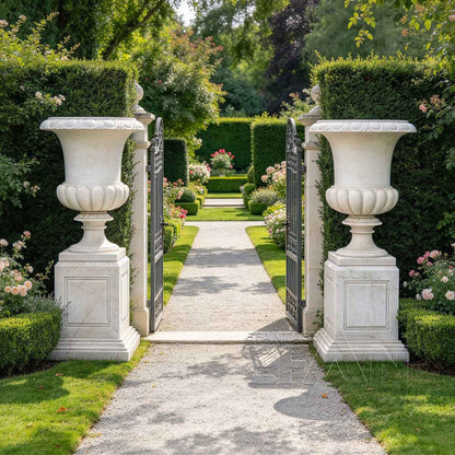 Two white marble flower pots on square pedestals beside a formal garden gate