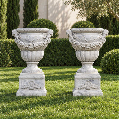 Pair of white marble urn planters with floral garland reliefs in a formal garden