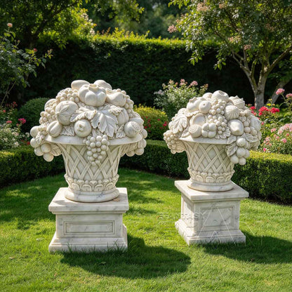 Pair of carved white marble fruit baskets with grape clusters in a garden setting